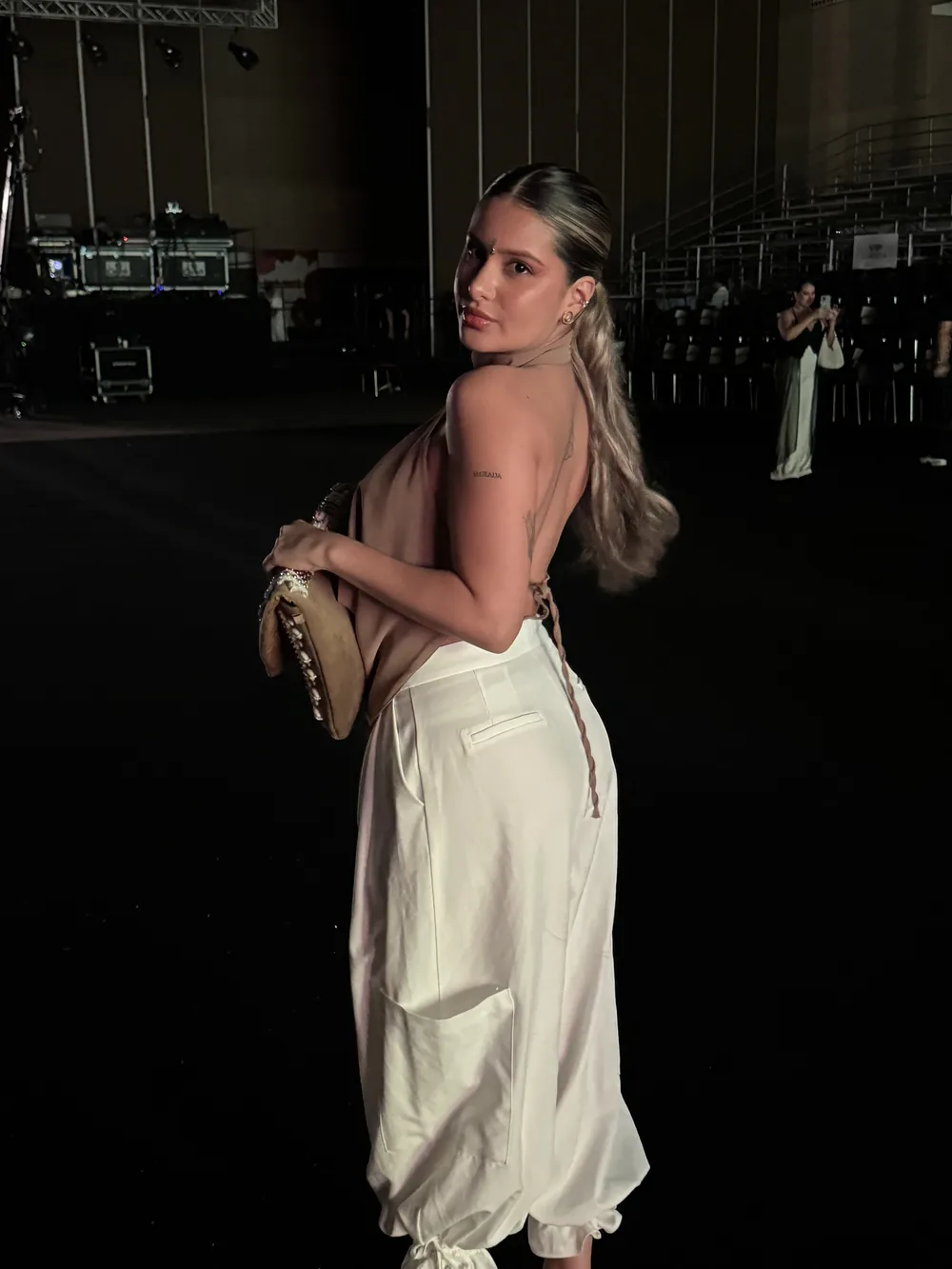 Brielah de espaldas, con pantalón blanco, mirando por encima del hombro en la noche